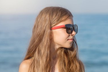 Close-up portrait of a girl in a bathing suit and glasses on the background of the sea shore. clipart