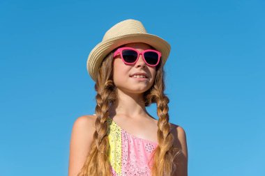 Close-up of a smiling young girl in a summer hat, against the sky.
