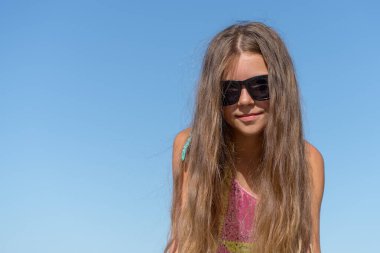 Portrait of a girl in sunglasses against the blue sky. Copy space.