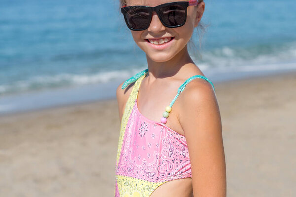 Girl in a pink bathing suit on the sea during the holidays. Large portrait.