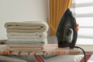 A pile of towels and an iron on the ironing board. Homework concept.