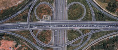 Metropolis 'teki çoklu şeritli otoyolun kavşağındaki insansız hava aracının yukarıdan görünüşü. Otobanlarda yoğun trafik var. Yüksek kıvrımlı yollar, yonca şekilli köprü hız sınırı yok..