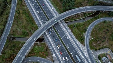 Metropolis 'teki çoklu şeritli otoyolun kavşağındaki insansız hava aracının yukarıdan görünüşü. Otobanlarda yoğun trafik var. Yüksek kıvrımlı yollar, yonca şekilli köprü hız sınırı yok..