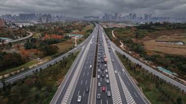 Yüksek gökdelenleri ve yükseltilmiş modern yonca yapraklı trafik kavşağı olan Chengdu şehir manzarasının insansız hava aracı görüntüsü. Sisli şehirde koyu gri gökyüzü, gelişmiş metropol Çin şehrinde yoğun trafik. Gündüz.