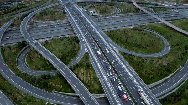 Сверху вниз с беспилотника на современном транспортном узле многополосной автомагистрали в мегаполисе. Пробки на автомагистралях. Высокие изогнутые дороги, мост в форме клевера без ограничения скорости.