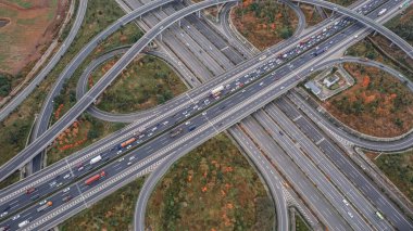 Metropolis 'teki çoklu şeritli otoyolun kavşağındaki insansız hava aracının yukarıdan görünüşü. Otobanlarda yoğun trafik var. Yüksek kıvrımlı yollar, yonca şekilli köprü hız sınırı yok..