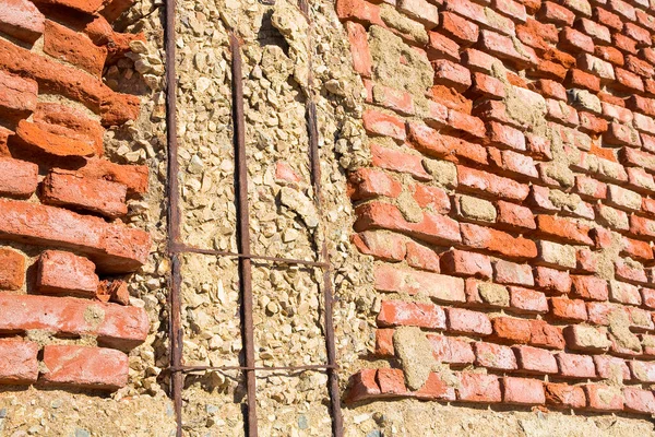 Old reinforced and dangerous concrete structure with damaged and rusty metallic reinforcement bars against a weathered and damaged brick wall.