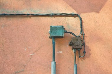 Eski elektrik ve telefon kabloları metal koruma kutusuyla sıva duvarına sabitlenmiş.