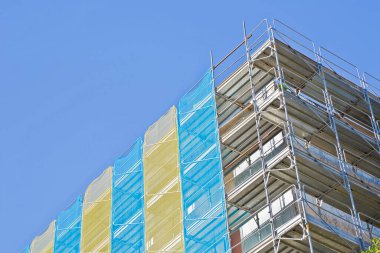 Alçı duvarın yenilenmesi ya da binanın enerji verimliliğini artırmak için termal yalıtımın gerçekleştirilmesi amacıyla bina cephesinde güvenle çalışmak üzere prefabrik bileşenlerle inşa edilmiş bir inşaat alanındaki metal yapı iskelesi..