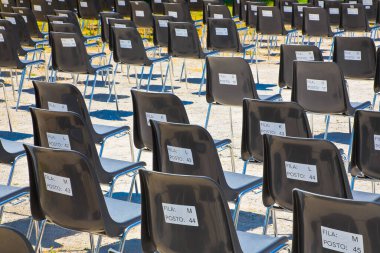 Coronavirus Sars-Cov-2 nedeniyle aralıklı siyah plastik koltuklu açık hava sineması - Koltukların arkasında koltuk numarası ve saygı duyulacak satır - FILA ham anlamına gelir - POSTO PLACE