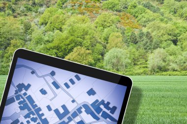Arazi yönetimi - satılık bir yerleşim alanındaki inşaat ve konut katmanı için kullanılabilir yeşil bir arazide boş bir araziyle emlak kavramı - hayali bir kadastro haritasıyla ön planda dijital tablet
