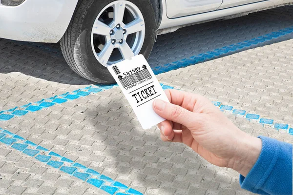 Female hand holds a parking ticket - parking payment concept with parked car