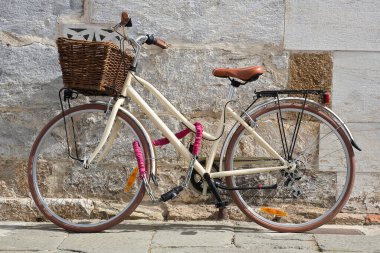 Women's bicycle with basket closed with chain against a wall in a italian street paved of stone 