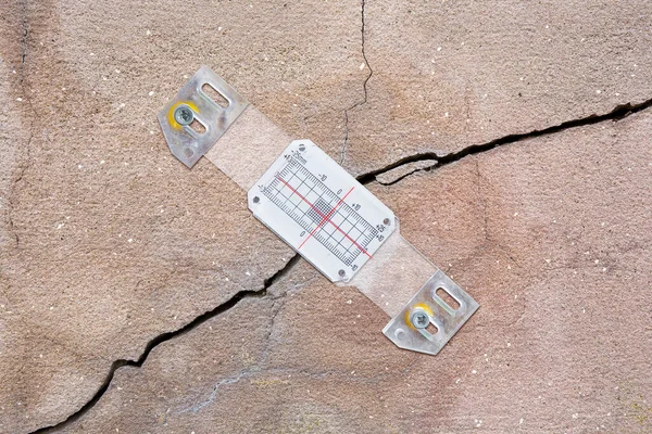 Deep crack in a damaged old plaster wall cause due to subsidence of foundations structural failures with plastic mechanical crack meter designed to measure movement across surface cracks and joints