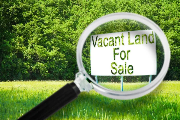 Advertising billboard immersed in a rural scene with Vacant Land for Sale written on it - concept image seen through a magnifying glass.