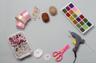 El yapımı eşyalar ve aletlerin üst görünümü, el işi, iğne işi: makas, yapıştırıcı tabancası, boncuklar, boncuklar, iplikler, ahşap mandallar. DIY, dikiş dersleri. Saten kurdeleler. Gri arka planda..