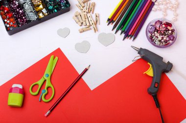 Sevgililer Günü 'nde, arka planda renkli kalemler, tahta mandallar, çakıl taşları, makas, kağıt, yapıştırıcı, rende, yağ tabancası, kupa desenleri. Kalpleri dekore et. Adım adım. Kendin yap.