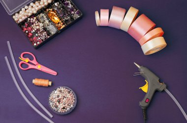 El aletleri koyu mor bir arka plana göre ayarlanmış. Saten pembe kurdeleler, yapay elmaslar, boncuklar, makas, tutkal tabancası, iplikler, yapıştırıcı çubukları. DIY. El yapımı. İğne işi dersleri..