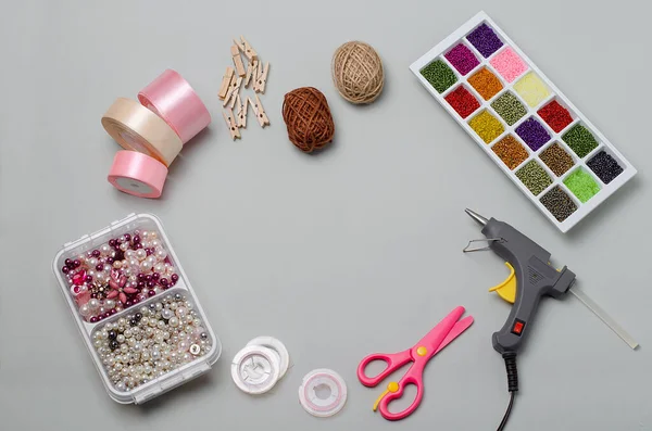 El yapımı eşyalar ve aletlerin üst görünümü, el işi, iğne işi: makas, yapıştırıcı tabancası, boncuklar, boncuklar, iplikler, ahşap mandallar. DIY, dikiş dersleri. Saten kurdeleler. Gri arka planda..