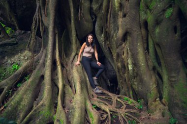 Genç bir kadın, tropik ormandaki dev kök ağacında yavrusuyla poz veriyor. Güneşli bir günde yeşil ormandaki kadın ve evcil hayvan. Sürdürülebilir turizm kavramı. Amatlan, Meksika