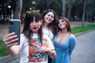 Ormanda yürüyen üç genç Latin bayan arkadaş. Birbirinize sarılın ve gülün. Arkadaşlar selfie çekiyor. Üç güzel Latin kadın selfie çekiyor.