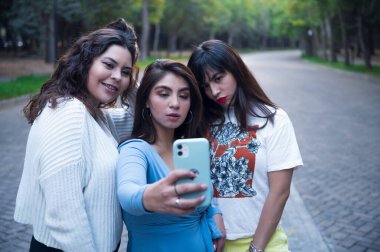 Ormanda yürüyen üç genç Latin bayan arkadaş. Birbirinize sarılın ve gülün. Arkadaşlar selfie çekiyor. Üç güzel Latin kadın selfie çekiyor.