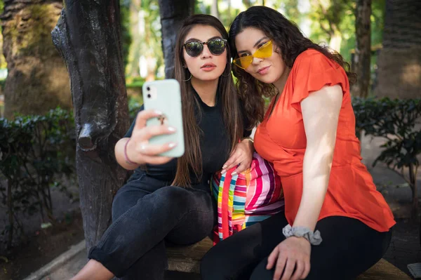 Two young latin female friends walking at the woods. Embrace each other and laughing. Friends making selfie. Two beautiful latin young women making selfie
