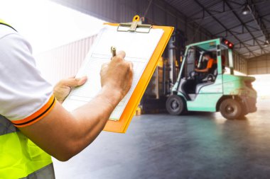 İşçi, kargo konteynırlarına paketleme kutularının yüklenmesini kontrol eden bir pano tutuyor. Tedarik zinciri. Forklift çekici kamyonları rıhtım deposuna yükleniyor. Kargo Sevkiyatı.