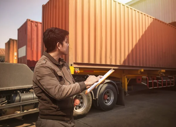 Worker Holds a Clipboard Controlling the Loading of Cargo into Shipping containers. Trucks Parked Loading at Dock Distribution Warehouse. Freight Truck Cargo Transport Logistics.