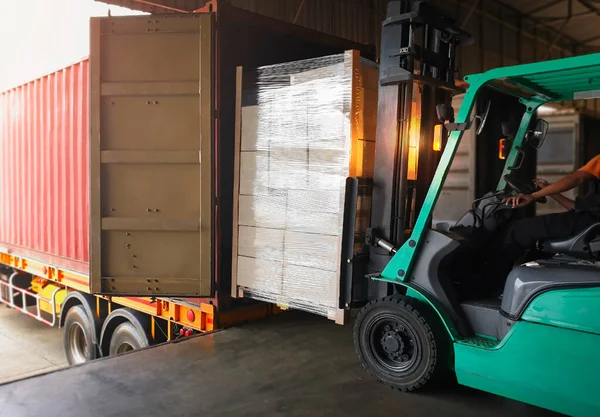 Forklift Tractor Loading Packaging Boxes into Shipping Container. Trucks Loading Dock Warehouse. Delivery Cargo Trucks. Distribution Warehouse Logistics. Cargo Shipment. Freight Truck Transport.