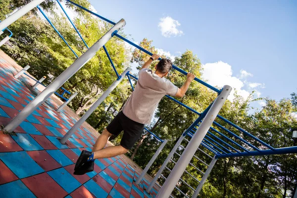 Ein Mann mit schwarzen Haaren treibt an einem warmen, sonnigen Tag Sport an der Querstange im Park. — Stockfoto