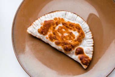 Kızarmış cheburek beyaz arka planda kahverengi bir tabakta yatıyor..