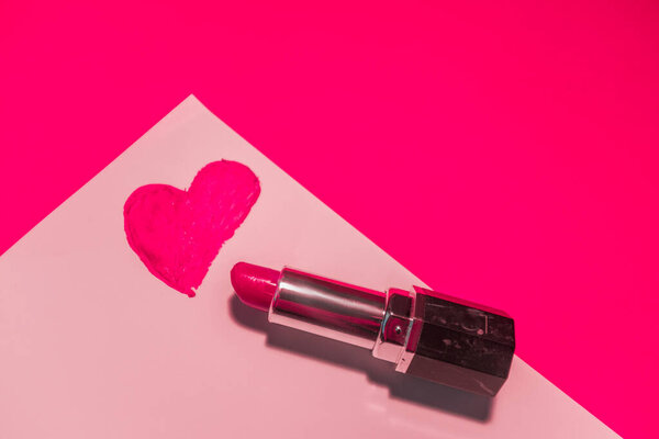 Сердце окрашено розовой помадой на белом листе на розовом фоне.