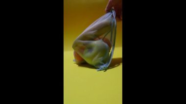  Sarı arka planda tek kullanımlık poşetteki meyveler. Dikey video