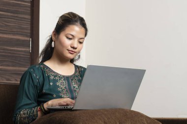 Genç Hintli etnik kız serbest çalışan kanepede oturup bilgisayar ekranına bakarak online problem çözme ve düşünme üzerine odaklanmış..