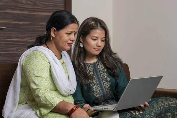 Indian mother and daughter watching into the laptop at home. Modern daughter helping her mother with technology. Mother and daughter at home.