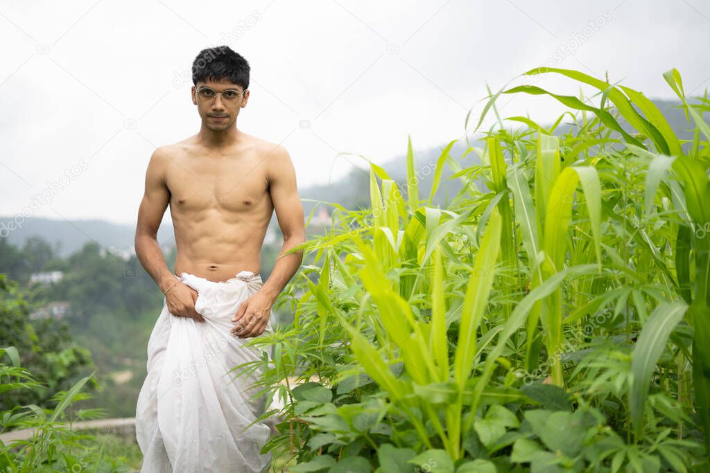 Young Indian fit boy, walking on a pathway beside crops in the field. An Indian priest walking while wearing white dhoti. Indian religious man.