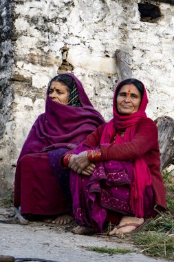 Almora, Uttarakhand - 3 Ocak 2022 - Yolda oturan ve kameraya bakan iki Hintli yaşlı kadın. Hint kıyafetleri giyen geleneksel Hintli kadınlar.