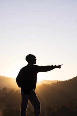 Silhouette of a young boy standing in the fields and the beautiful mountains in the background captured during sunset.