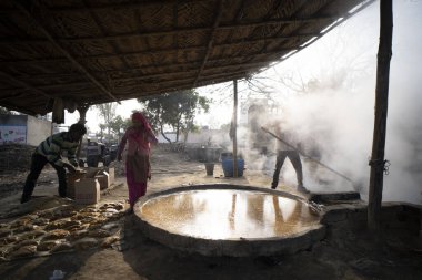 Delhi, Hindistan - 12 Ocak 2022 - Hintli erkekler Uttar Pradesh 'te şeker kamışı suyundan jaggery yapıyorlar. Köylerde küçük işletmelerde çalışan adamlar.