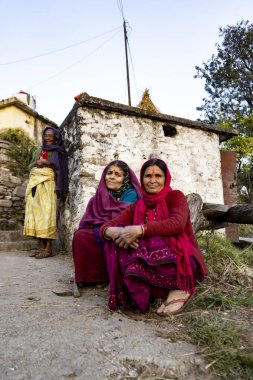 Almora, Uttarakhand - 3 Ocak 2022 - Yolda oturan ve kameraya bakan iki Hintli yaşlı kadın. Hint kıyafetleri giyen geleneksel Hintli kadınlar.