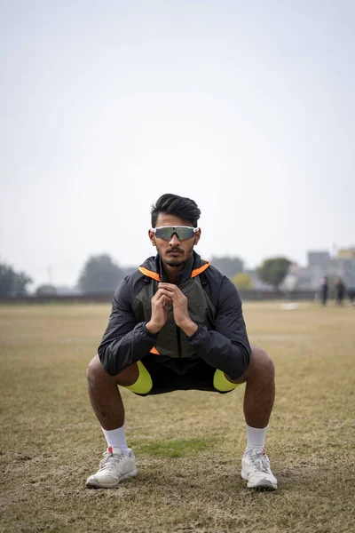 スポーツウェアを着たインドの少年が現場でスクワットをしているのを正面から撮影した スポーツとライフスタイルのコンセプト — ストック写真