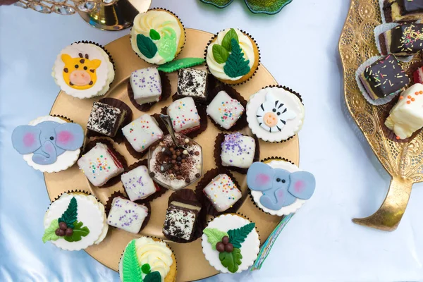 Hayvan şeklinde koyu ve beyaz çikolatalı kekler ve yuvarlak bir tabakta yapraklar, etrafında daha fazla çeşit kapkek var.