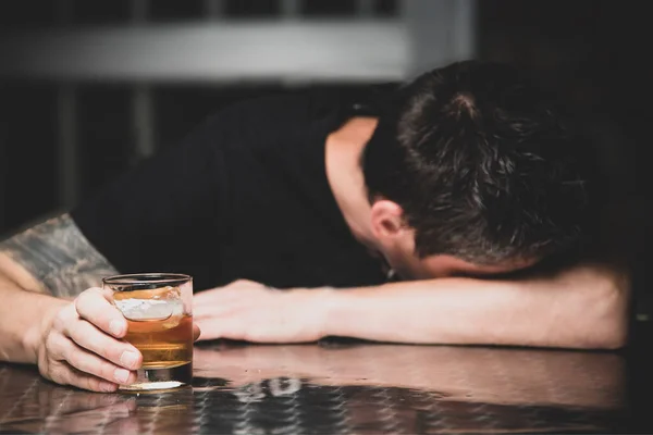Elinde bir bardak viskiyle bar masasında uyuyan sarhoş adam.