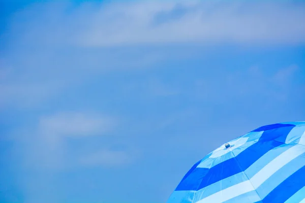 Fotoğrafın sağ tarafında mavi kumsal şemsiyesi, arka planda mavi gökyüzü.