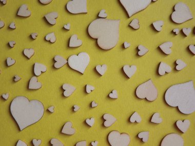 Sarı arka planda farklı boyutlarda tahta kalpler. Sevgililer Günü, bir aşk ilanı