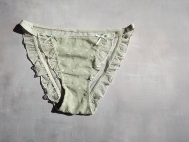 Açık yeşil kadın külotu ve gri bir arka planda fırfırları var.
