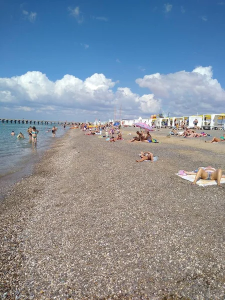 Erkekler ve kadınlar bulutlu havada plajda dinlenirler.