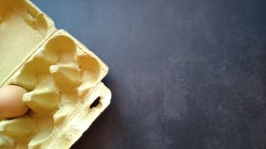 Bir kadının eli yumurta kutusundan bej bir yumurta alır.