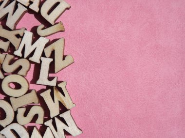 Arkaplan olarak pembe süet üzerine İngiliz alfabesinin ahşap harfleri